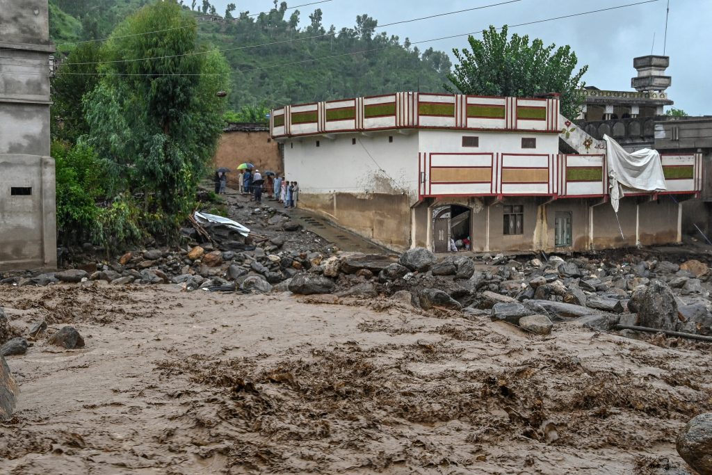 Villagers (center, L) stand near a building as floodwater levels rise in the Buner district of Pakistan's Khyber Pakhtunkhwa province on August 18, 2025.